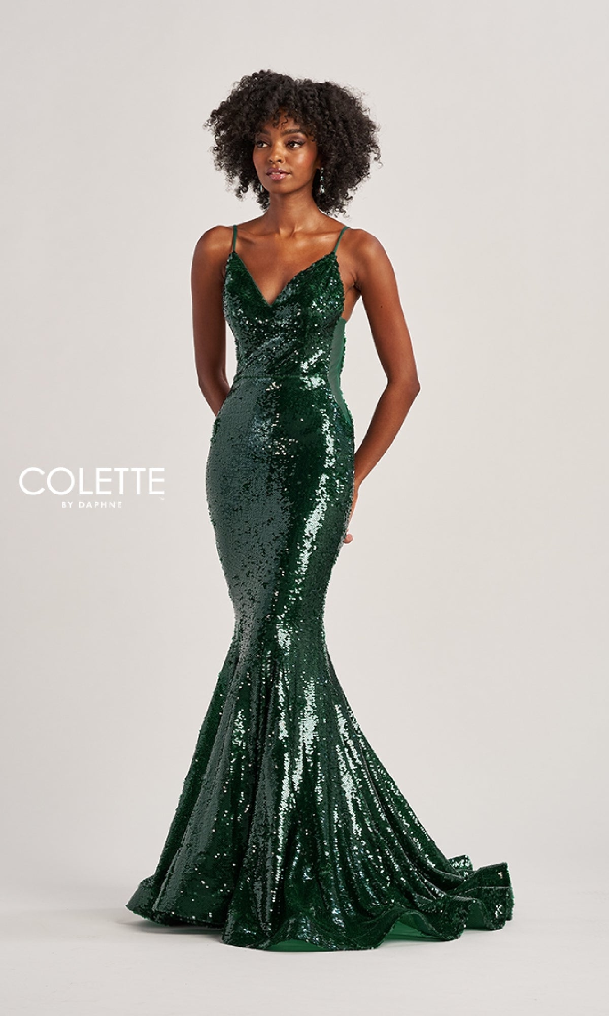 A woman wears a fitted, floor-length green Long Prom Dress: Colette CL8615 with thin straps, standing against a plain light background.